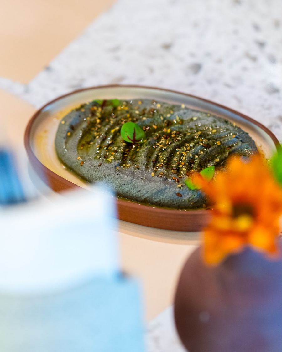 A herb dip glossed with olive oil and seeds, beside an orange flower