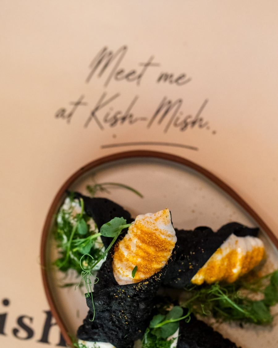 Charcoal pastry with whipped cheese beside the words “Meet me at Kish-Mish”