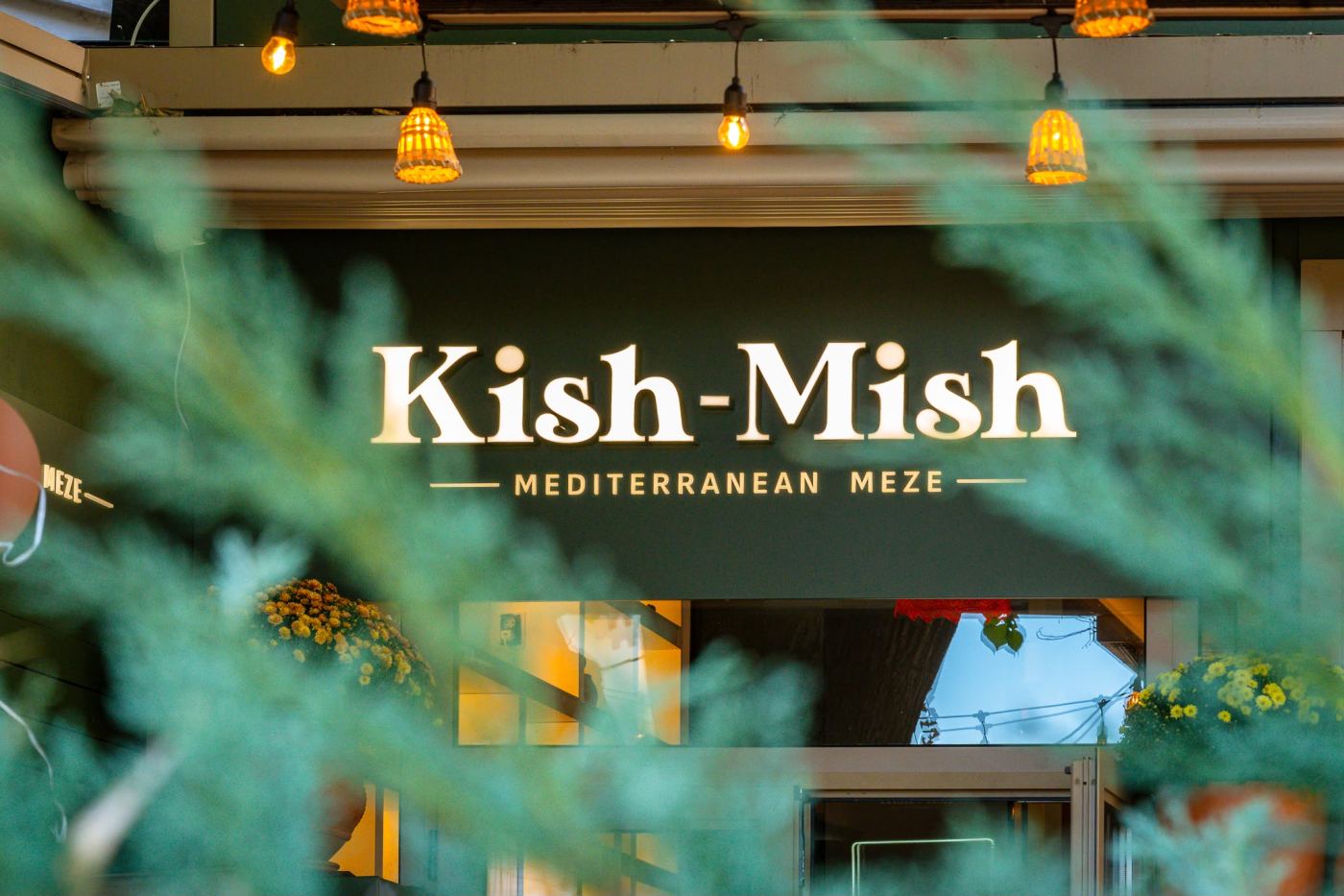 The illuminated Kish-Mish sign seen through green branches